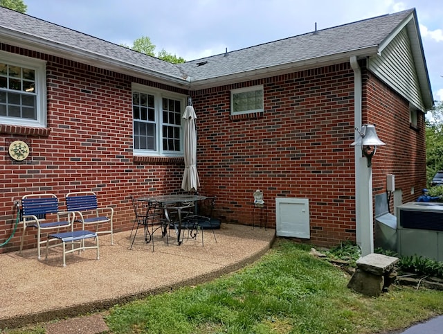 rear view of house featuring brick siding, a shingled roof, and a patio