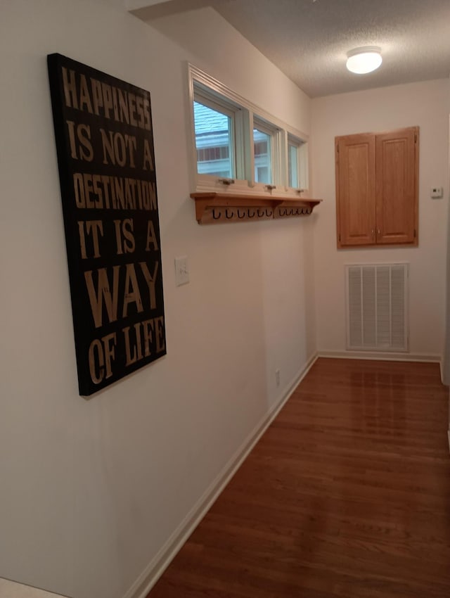 hallway with visible vents, a textured ceiling, baseboards, and dark wood-type flooring