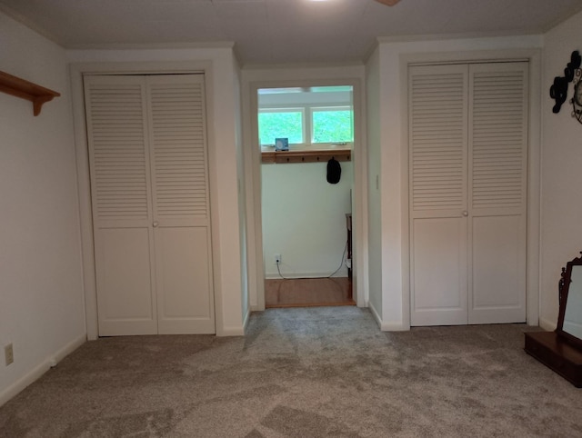unfurnished bedroom with baseboards, ornamental molding, carpet, and two closets