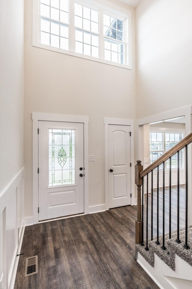 foyer entrance featuring a high ceiling, visible vents, plenty of natural light, and dark wood finished floors