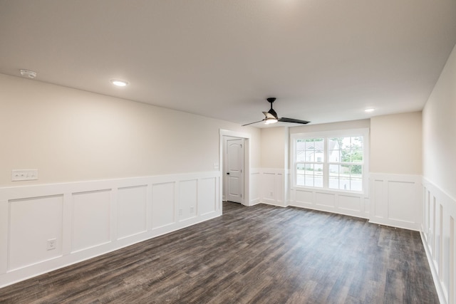 unfurnished room featuring wainscoting, a decorative wall, a ceiling fan, and dark wood-style floors