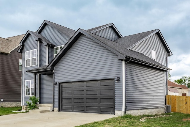 view of side of property with fence, driveway, roof with shingles, and a garage