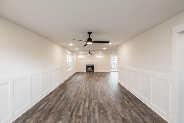 unfurnished living room with a ceiling fan, a decorative wall, a healthy amount of sunlight, and dark wood-style floors