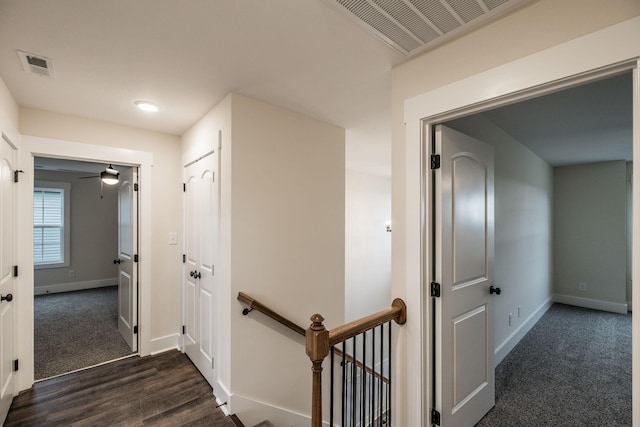 corridor featuring visible vents, baseboards, dark wood-style flooring, and an upstairs landing