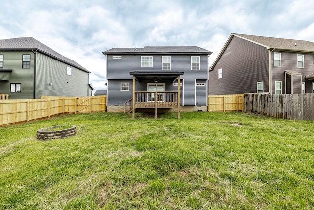 back of house with a fenced backyard, a wooden deck, a lawn, and a fire pit