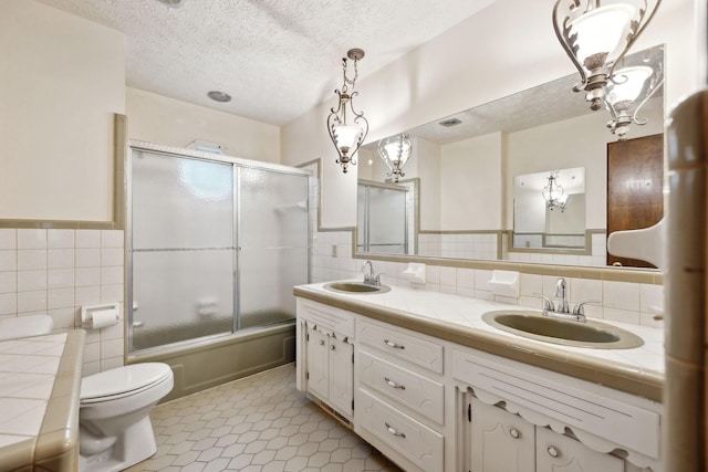 full bath featuring a sink, tile walls, toilet, and double vanity