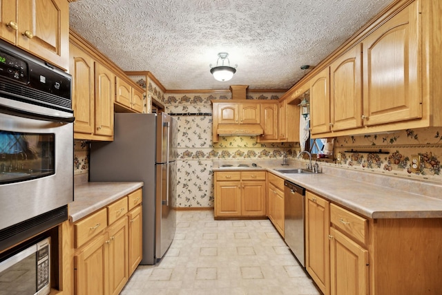 kitchen with appliances with stainless steel finishes, a sink, light countertops, brick patterned floor, and wallpapered walls