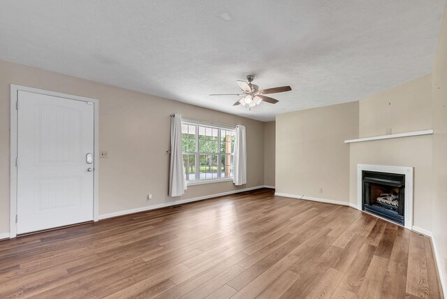 210 Edgewood Dr, Hohenwald, TN 38462 - unfurnished living room with ceiling fan, a fireplace, a textured ceiling, baseboards, and light wood-type flooring
