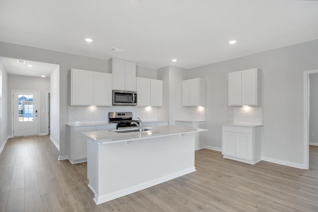kitchen featuring light wood-style floors, baseboards, a center island with sink, appliances with stainless steel finishes, and backsplash
