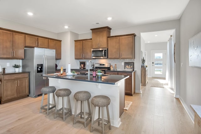 kitchen with brown cabinets, stainless steel appliances, dark countertops, and a sink