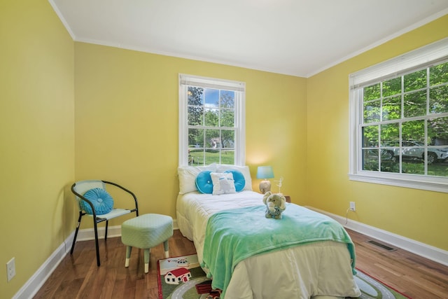 bedroom featuring baseboards, ornamental molding, wood finished floors, and visible vents