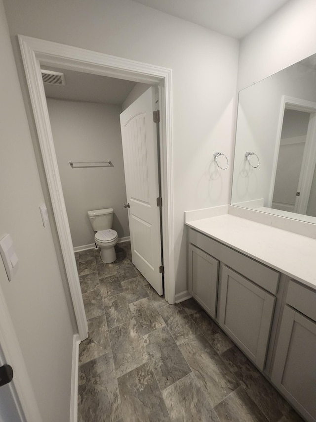 bathroom featuring vanity, toilet, baseboards, stone finish flooring, and visible vents