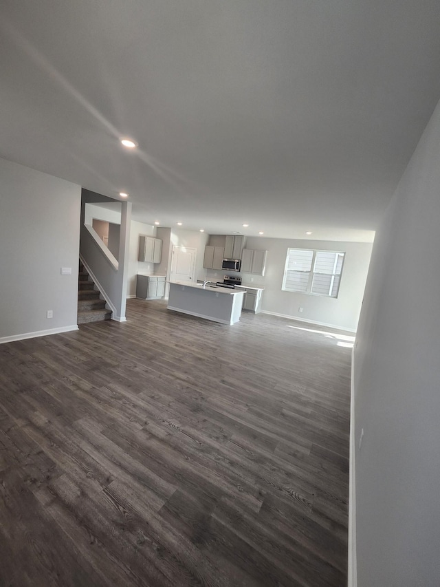 unfurnished living room featuring recessed lighting, baseboards, dark wood finished floors, and stairway