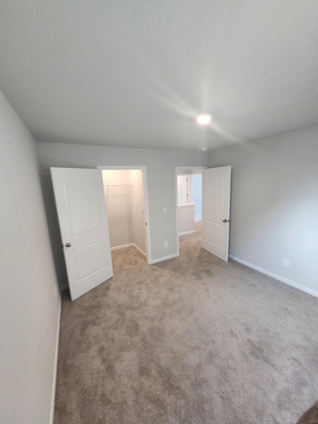 unfurnished bedroom with baseboards, a walk in closet, and carpet
