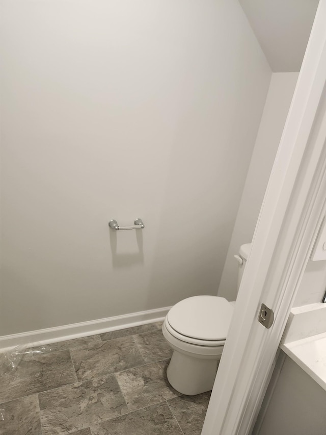 bathroom with baseboards, stone finish floor, and toilet