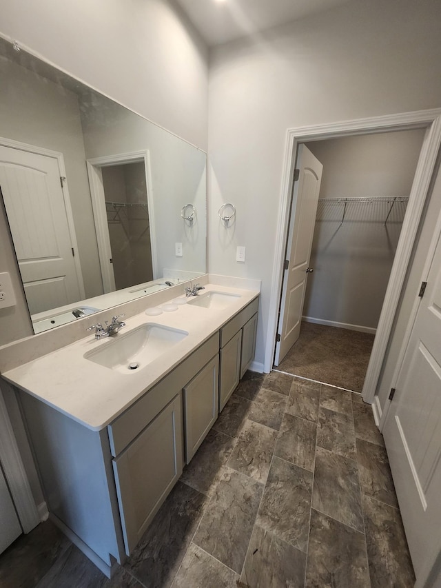 full bathroom featuring double vanity, baseboards, a spacious closet, and a sink