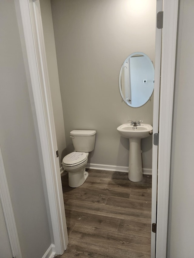 half bathroom with baseboards, wood finished floors, and toilet