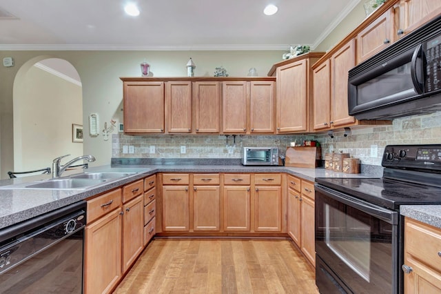 kitchen featuring crown molding, arched walkways, a sink, black appliances, and light wood-style flooring