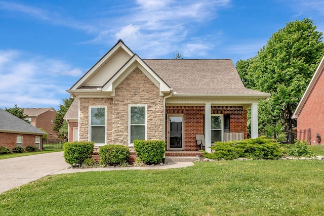 view of front of home featuring brick siding, fence, a front lawn, a shingled roof, and stone siding