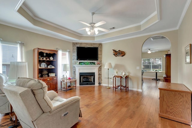 living area featuring ceiling fan, a raised ceiling, light wood-style floors, a large fireplace, and visible vents