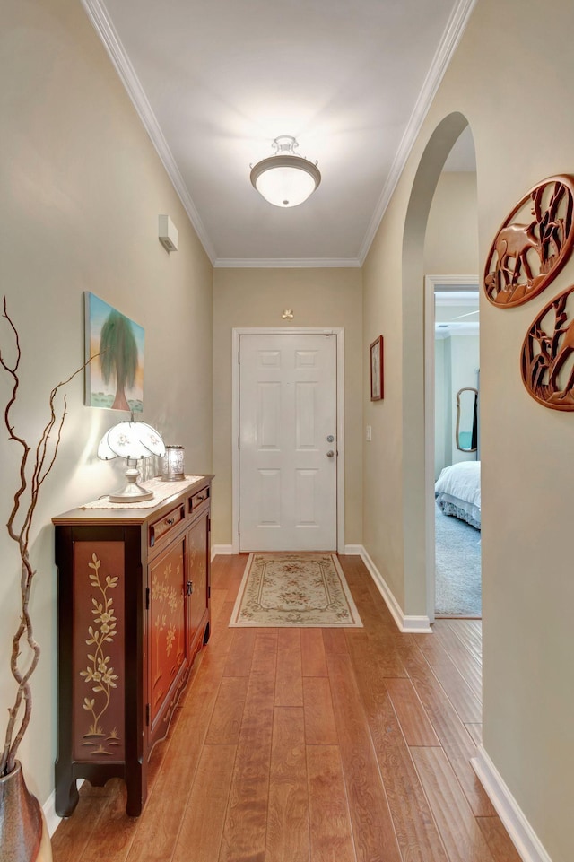 entryway with crown molding, arched walkways, and light wood finished floors