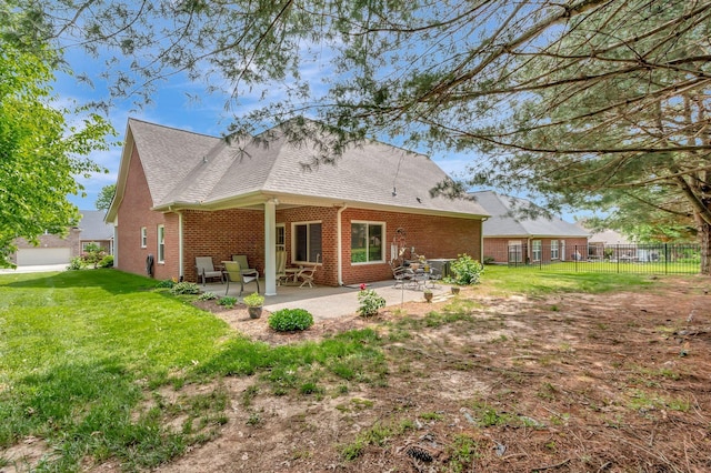 rear view of house with fence, a shingled roof, brick siding, a patio area, and a lawn