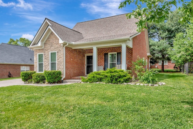 view of front of house featuring brick siding, roof with shingles, stone siding, and a front yard