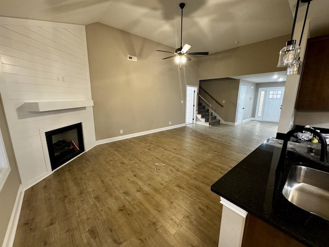 living room with a fireplace, a ceiling fan, wood finished floors, vaulted ceiling, and stairway