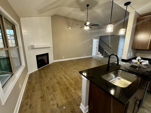 kitchen featuring wood finished floors, lofted ceiling, a fireplace, ceiling fan, and a sink