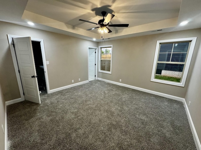 unfurnished bedroom with baseboards, a raised ceiling, visible vents, and dark colored carpet