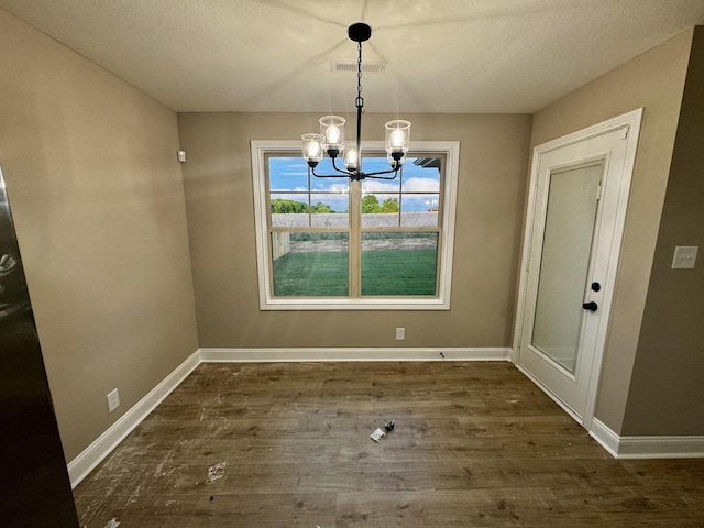 unfurnished dining area featuring visible vents, baseboards, wood finished floors, and a notable chandelier