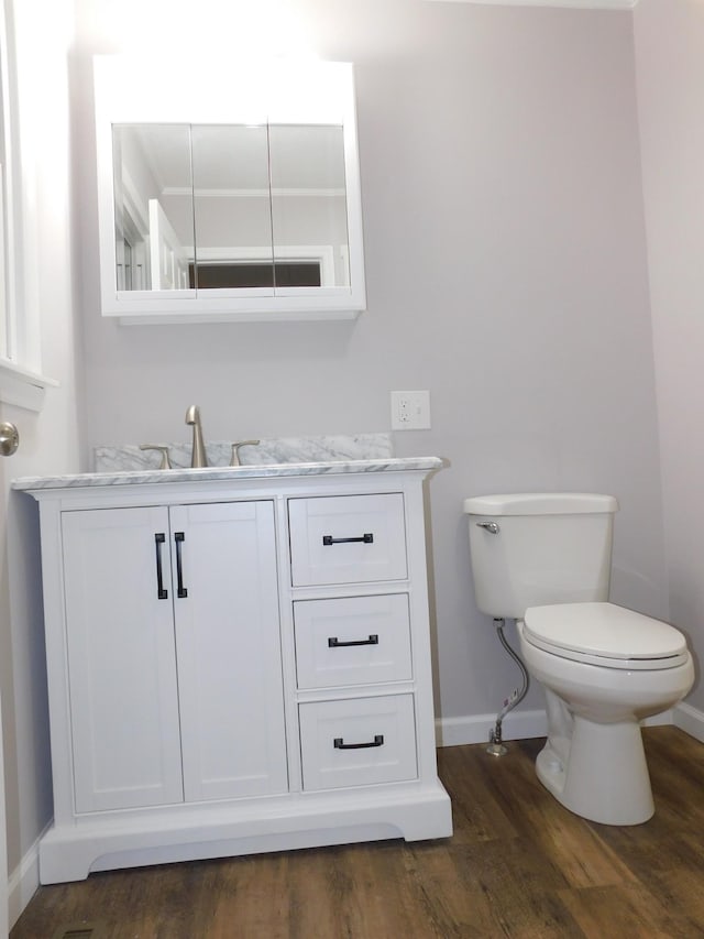 half bathroom featuring baseboards, wood finished floors, toilet, and vanity
