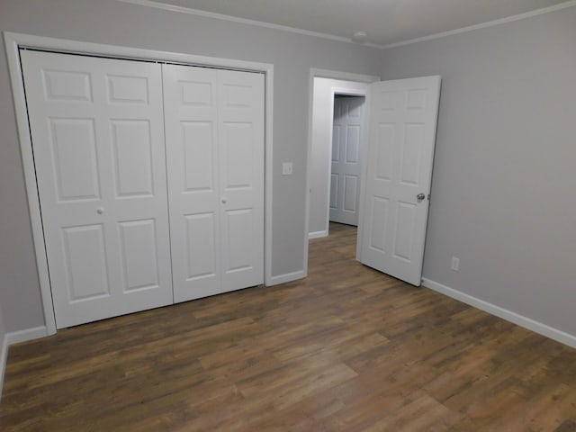 unfurnished bedroom with crown molding, baseboards, dark wood-style floors, and a closet