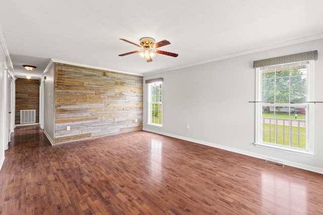 unfurnished living room with visible vents, wood walls, crown molding, and a wealth of natural light