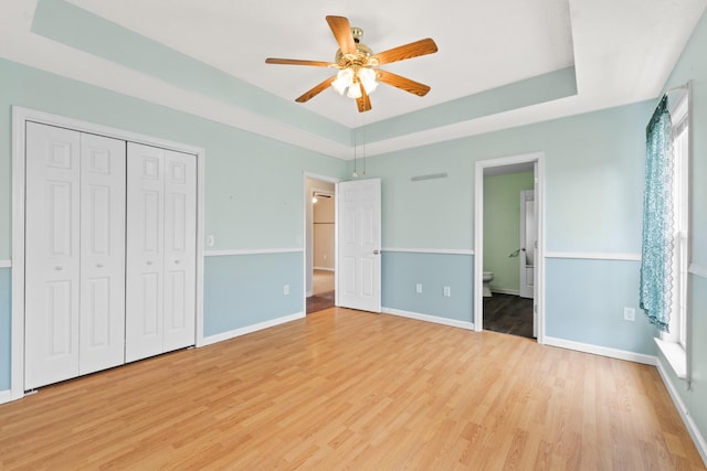 unfurnished bedroom with baseboards, light wood-style flooring, a raised ceiling, and a closet