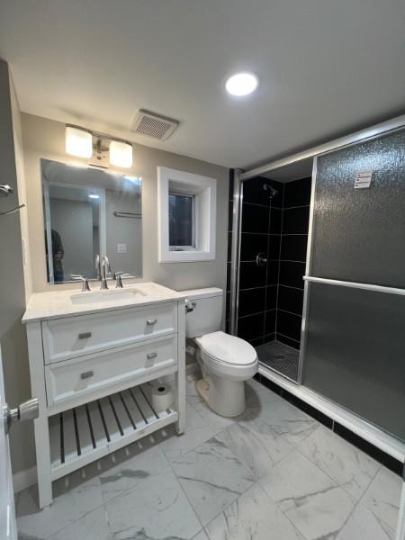 bathroom with vanity, toilet, marble finish floor, visible vents, and a stall shower