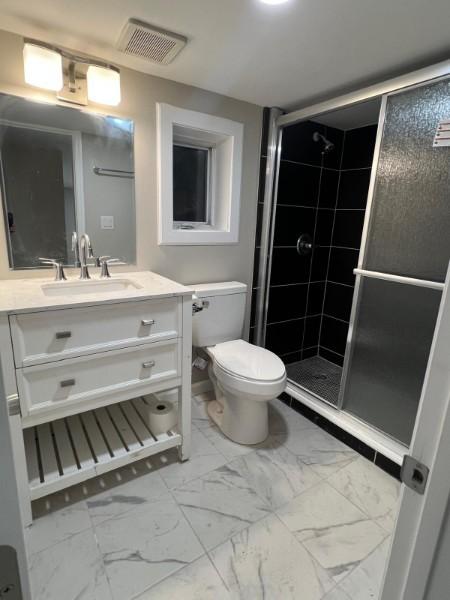 bathroom with vanity, toilet, marble finish floor, a shower stall, and visible vents