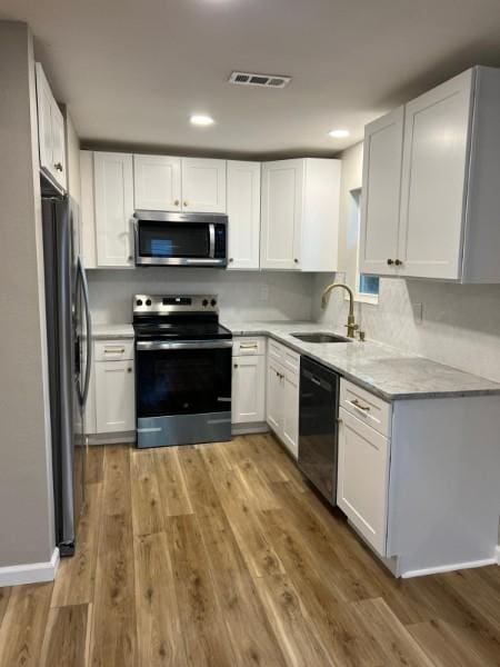 kitchen featuring visible vents, white cabinets, a sink, light wood-style flooring, and appliances with stainless steel finishes