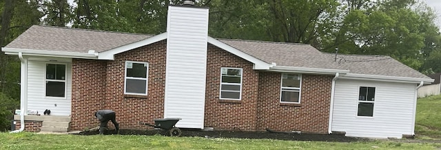 back of property with brick siding, a chimney, and a shingled roof