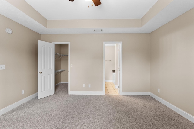 unfurnished bedroom with a walk in closet, visible vents, light colored carpet, baseboards, and a closet