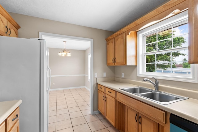 kitchen featuring a sink, light tile patterned floors, freestanding refrigerator, dishwashing machine, and an inviting chandelier