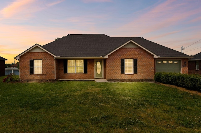 ranch-style home with a yard, brick siding, an attached garage, and roof with shingles