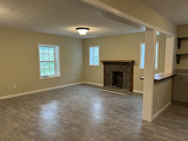 unfurnished living room featuring baseboards, a textured ceiling, dark wood-style floors, and a stone fireplace
