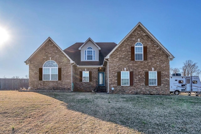 traditional home featuring fence, brick siding, and a front yard
