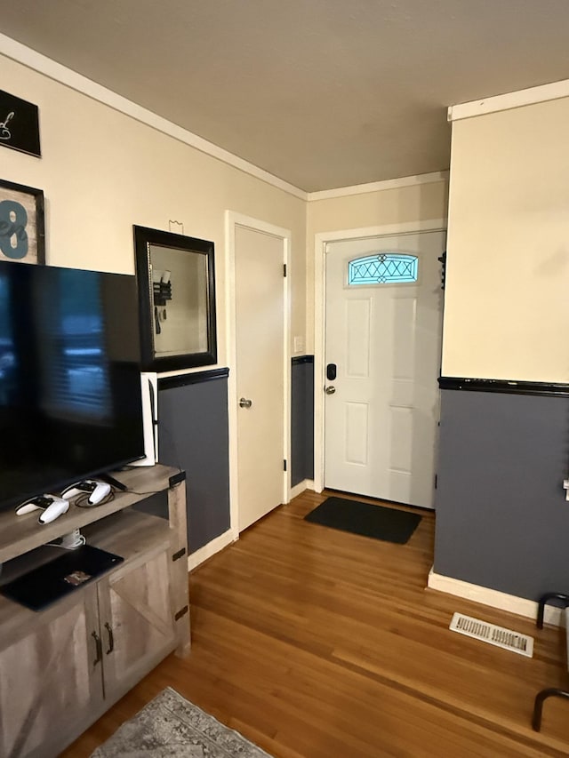 foyer featuring baseboards, ornamental molding, wood finished floors, and visible vents
