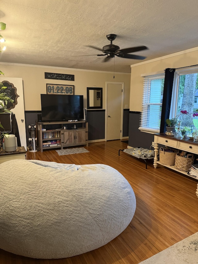 living area featuring a ceiling fan, a textured ceiling, ornamental molding, and wood finished floors