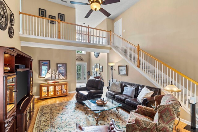 living area with light wood-type flooring, stairs, ceiling fan, and a towering ceiling