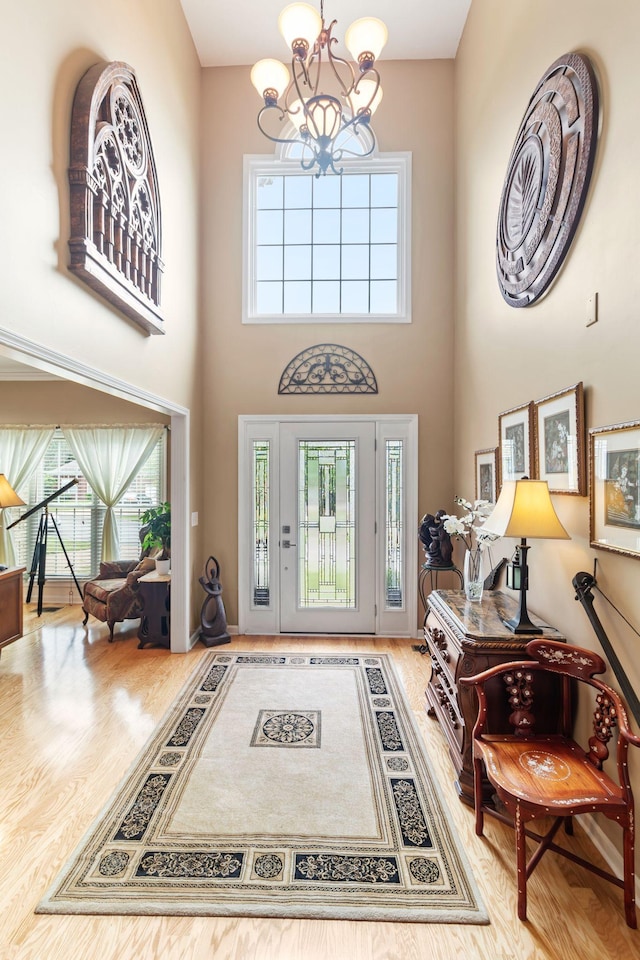 entryway with a notable chandelier, wood finished floors, and a towering ceiling