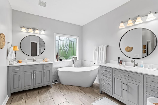 bathroom featuring visible vents, a sink, a freestanding bath, and two vanities
