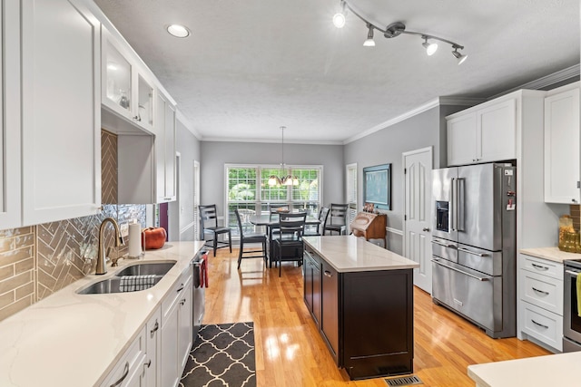 kitchen with appliances with stainless steel finishes, a sink, white cabinetry, decorative backsplash, and light wood-type flooring
